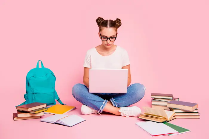 In this stock photo, a girl surrounded by text books studies with her laptop computer.